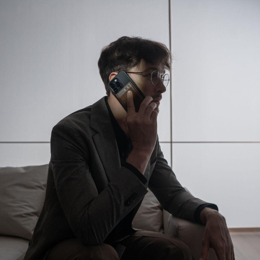 A man in a suit holds a smartphone with a gold Plaud Note attached to the back while sitting on a couch.