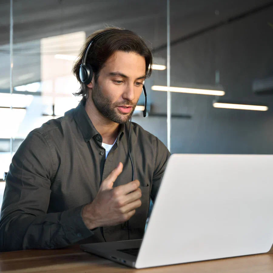 A man wearing a headset and using a laptop in an office, recording a meeting with a Plaud AI voice recorder.