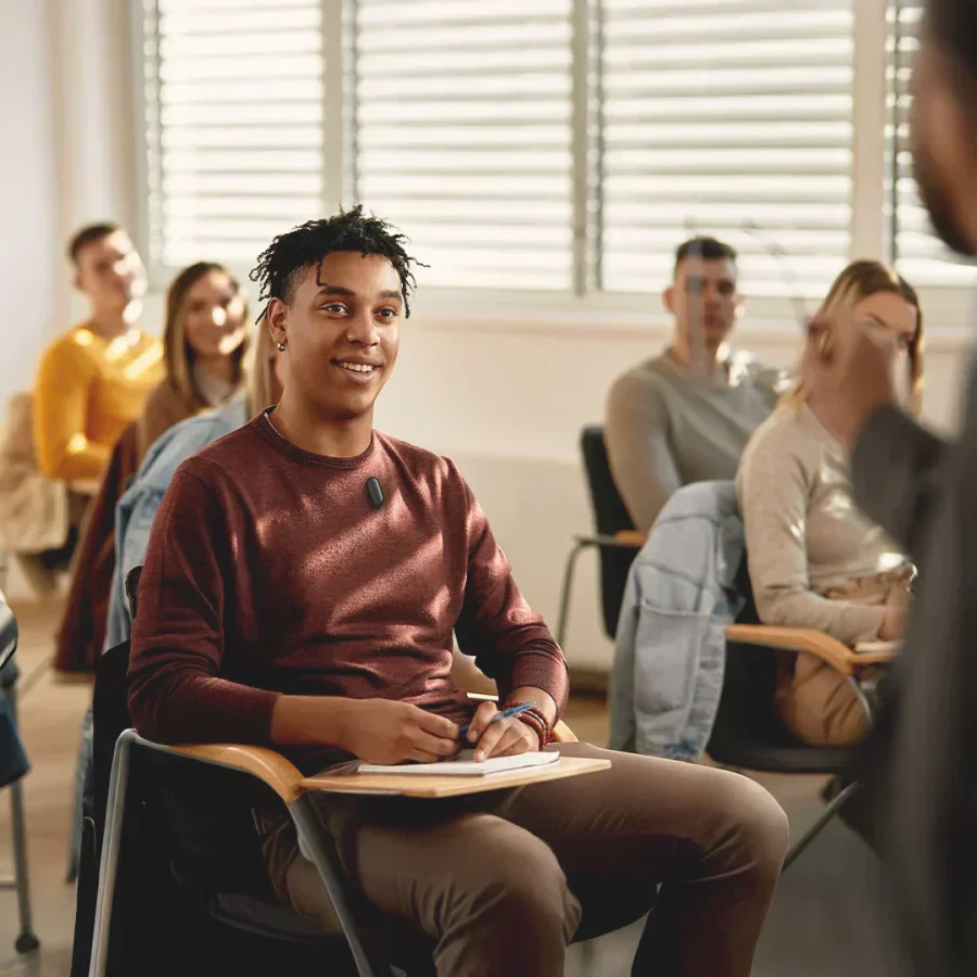 A student wearing a black Plaud NotePin on his sweater while attending a lecture in a classroom.