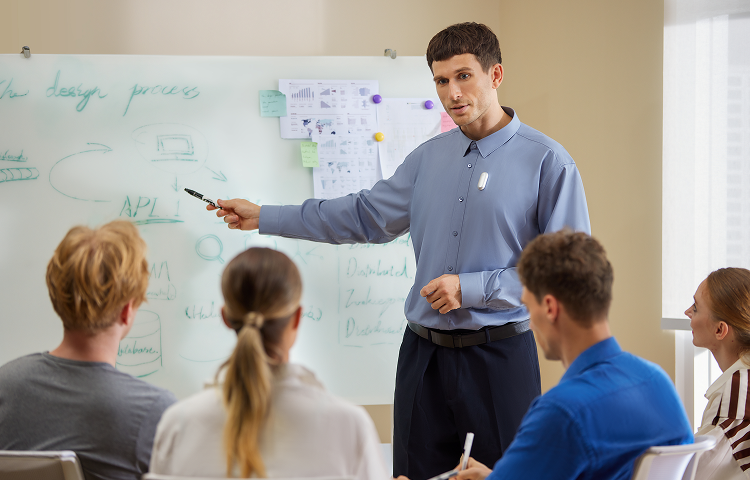 Man wearing a silver Plaud NotePin on his shirt leads a meeting in front of a whiteboard.