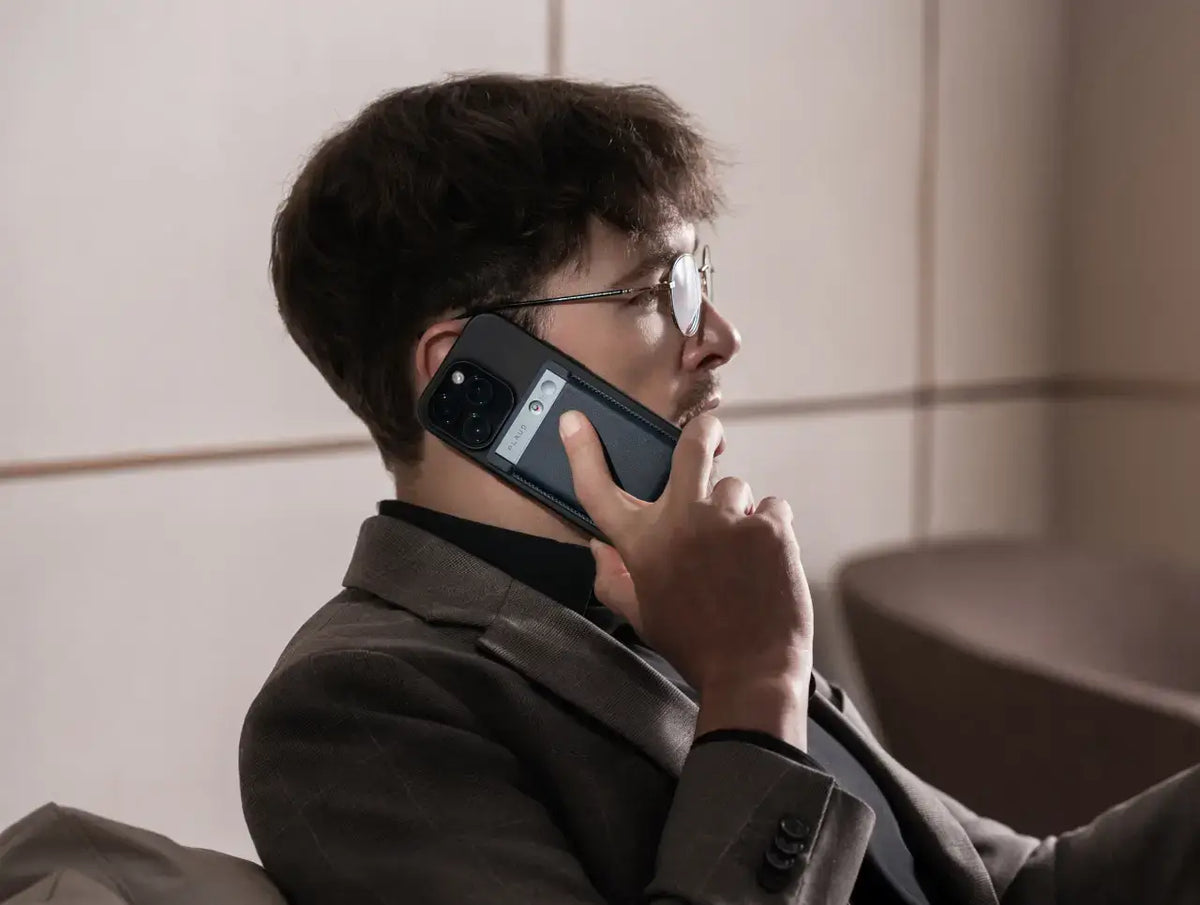 Man in a suit recording a phone call using a black Plaud Note attached to the back of his smartphone.