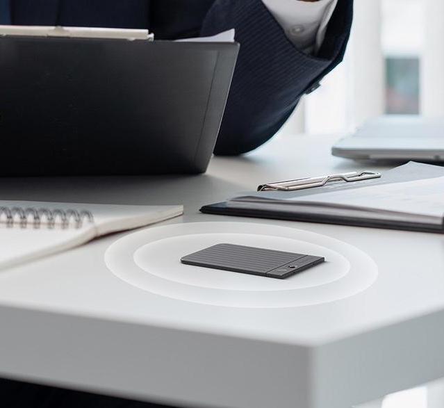 A black Plaud Note Pro on a white desk during a meeting, capturing audio with 360-degree sound waves.