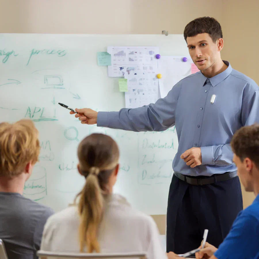 Man wearing a silver Plaud NotePin on his shirt while presenting at a whiteboard to a group.