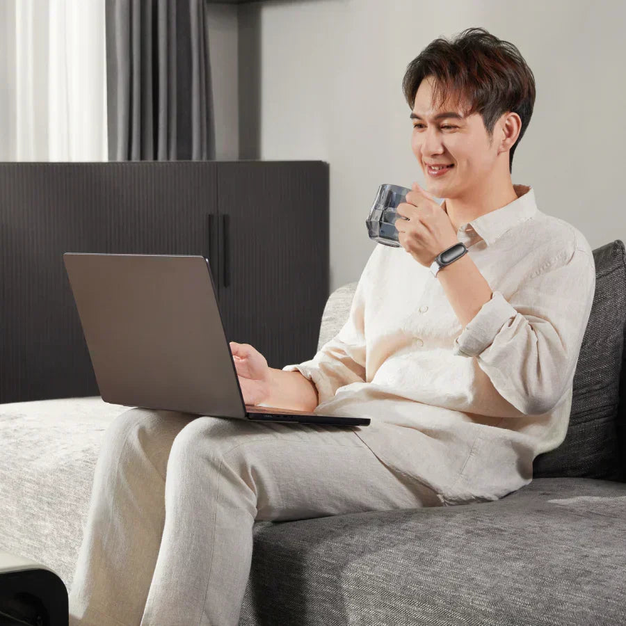 Man wearing a black Plaud NotePin on a wristband while working on a laptop.