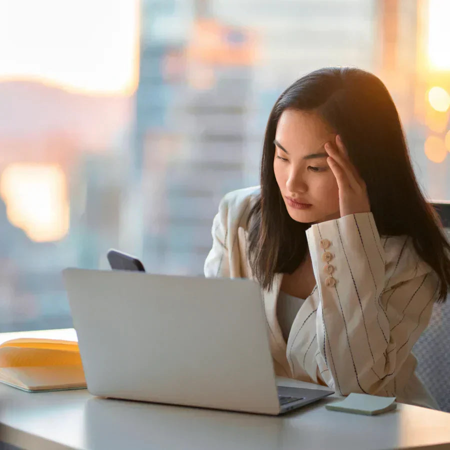 Focused woman at a desk wearing a silver Plaud NotePin on her striped blazer while working on a laptop.