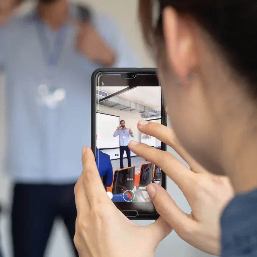 Person recording a presenter on a smartphone during a meeting.