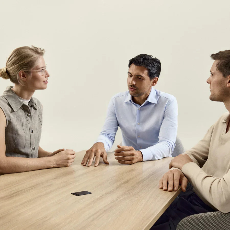 Three professionals discuss around a table with a black Plaud Note capturing the meeting.