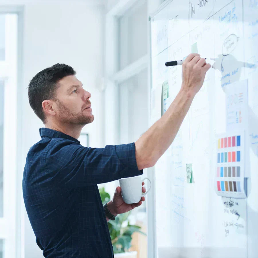 A man writes on an office whiteboard during a brainstorming session.