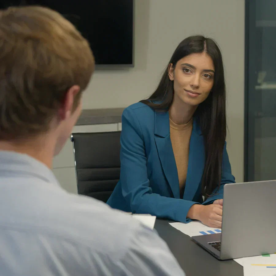 A woman in a blue blazer wearing a black Plaud NotePin on her lapel during a business meeting.