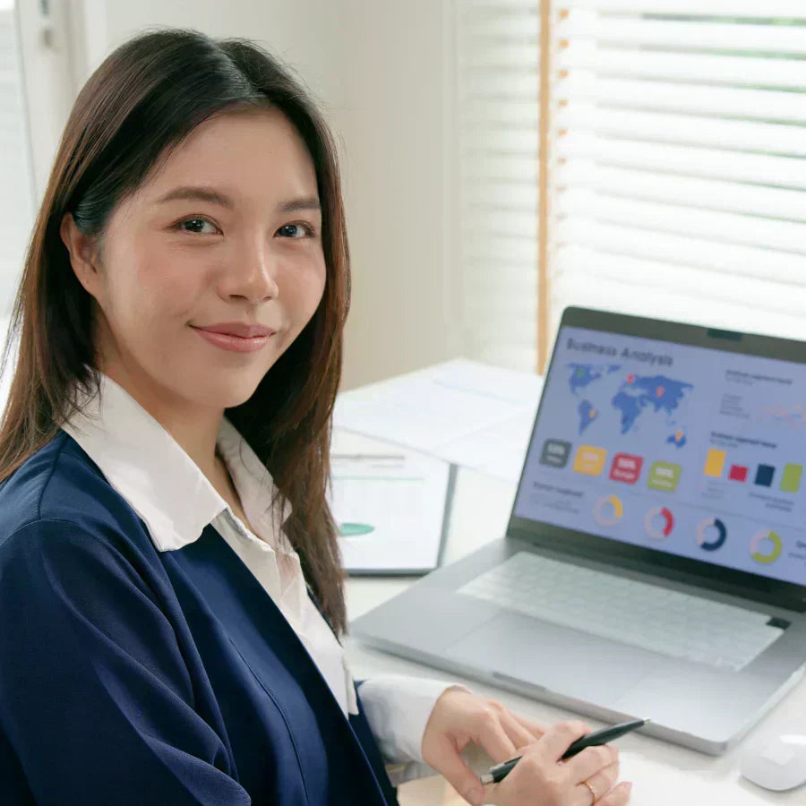 A professional woman at a desk with a laptop displaying a business analysis dashboard.