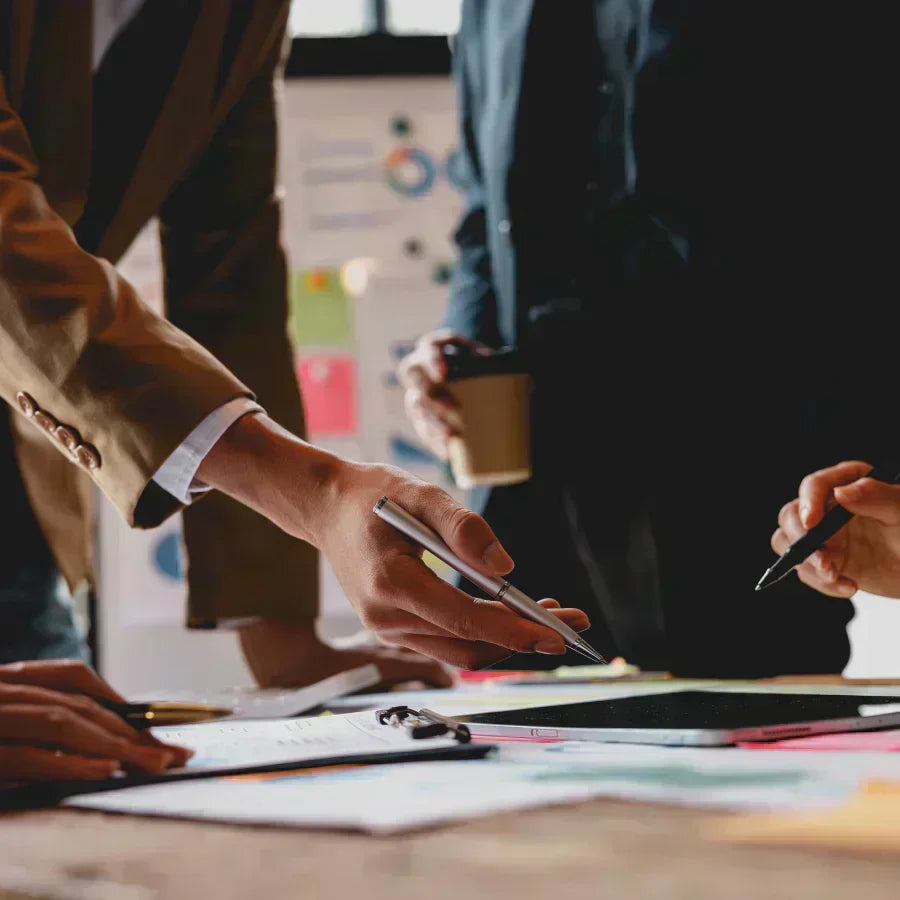 Professionals collaborating in a meeting, pointing at documents and a tablet on a desk.