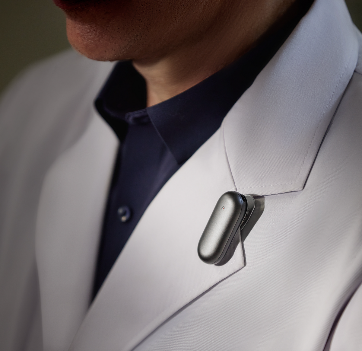 A Cosmic Gray Plaud NotePin clipped to the lapel of a white lab coat.