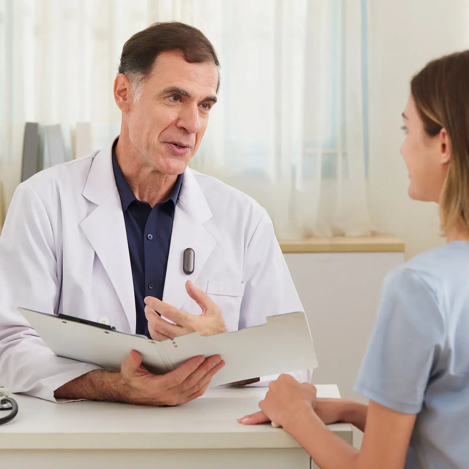 A doctor wearing a black Plaud NotePin on his lapel while speaking with a patient during a consultation.