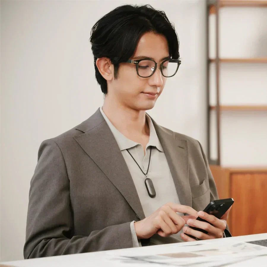 A man in a blazer wearing a Cosmic Gray Plaud NotePin on a lanyard while using his smartphone.
