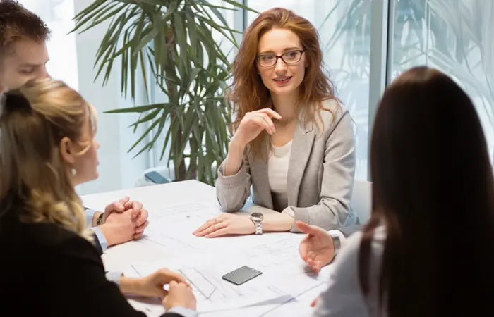 A black Plaud Note records a business meeting as a group of professionals discuss plans around a table.
