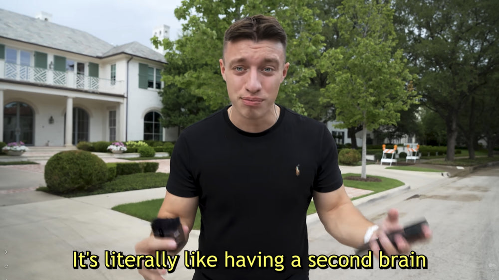 A man holds a Plaud AI voice recorder outdoors. Text: 'It's literally like having a second brain.'