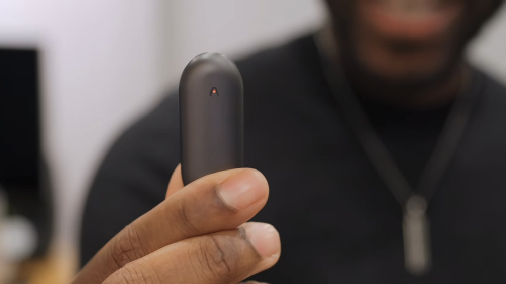 A person holds a small, black Plaud NotePin wearable AI voice recorder to demonstrate its compact size.