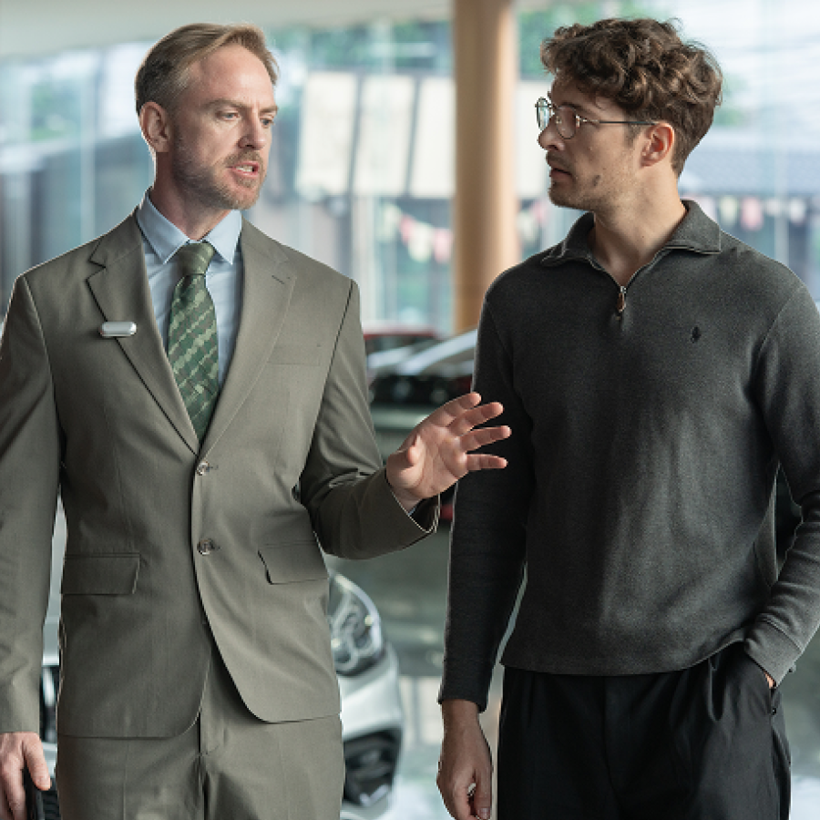 Professional in a suit wearing a silver Plaud NotePin while talking to a client in a car showroom.