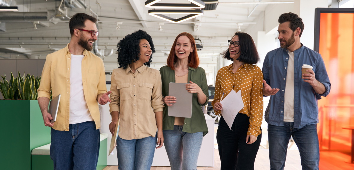 Five diverse professionals walking and laughing together in a bright, modern open-plan office.