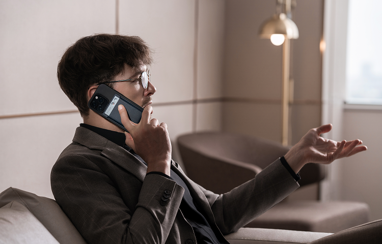Man in a suit using a black Plaud Note attached to his smartphone to record a phone call.