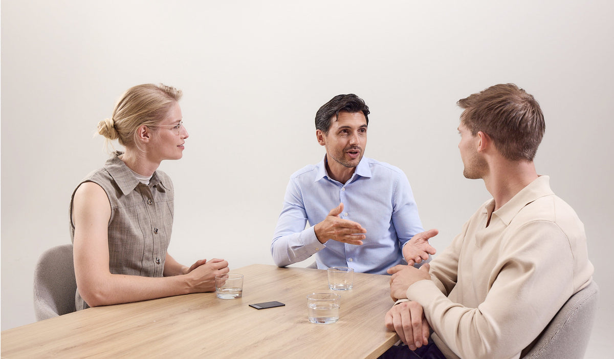 Three professionals in a meeting with a black Plaud Note on the table recording their conversation.
