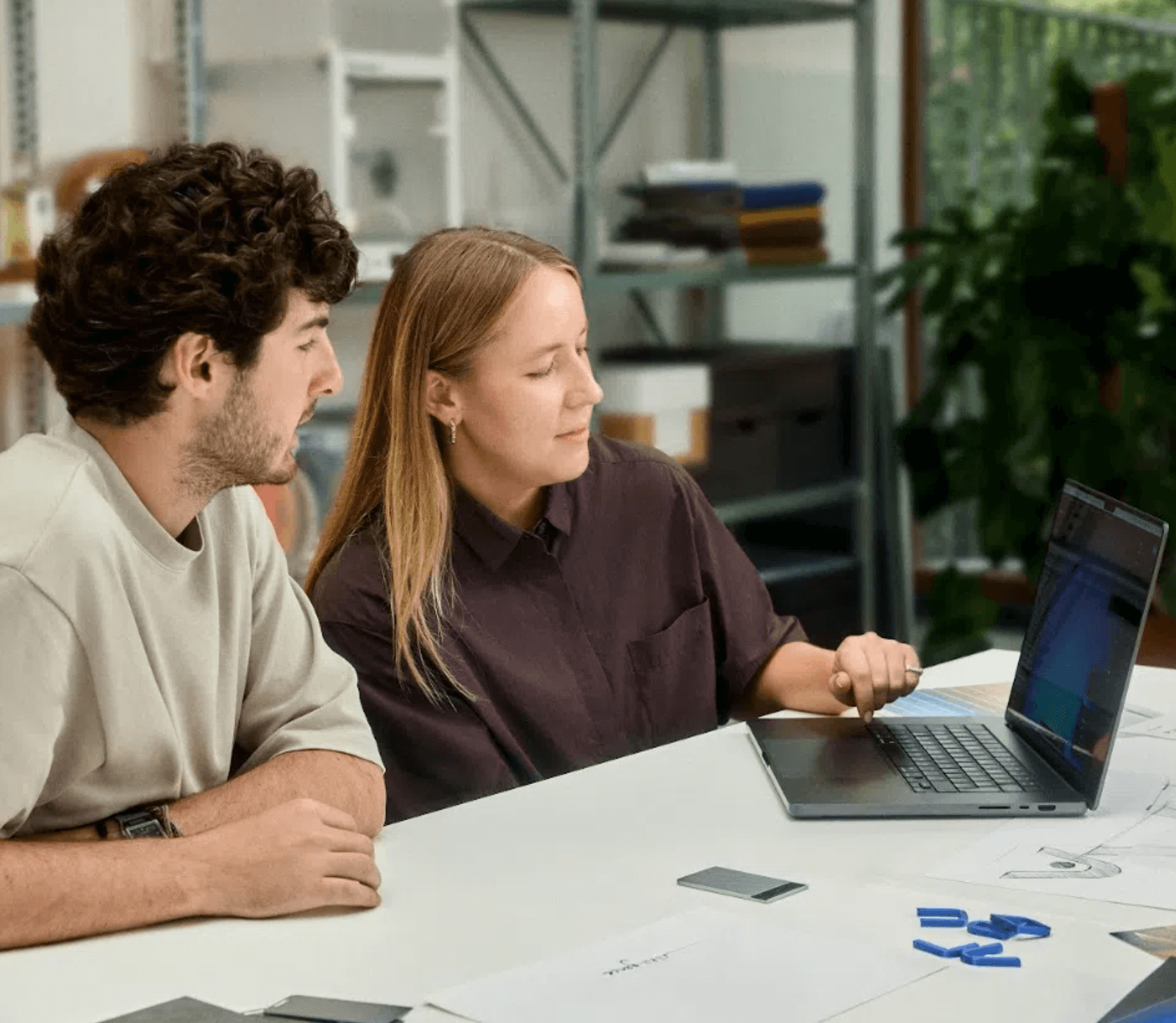 Two colleagues review data on a laptop with a silver Plaud Note on the desk in a studio setting.